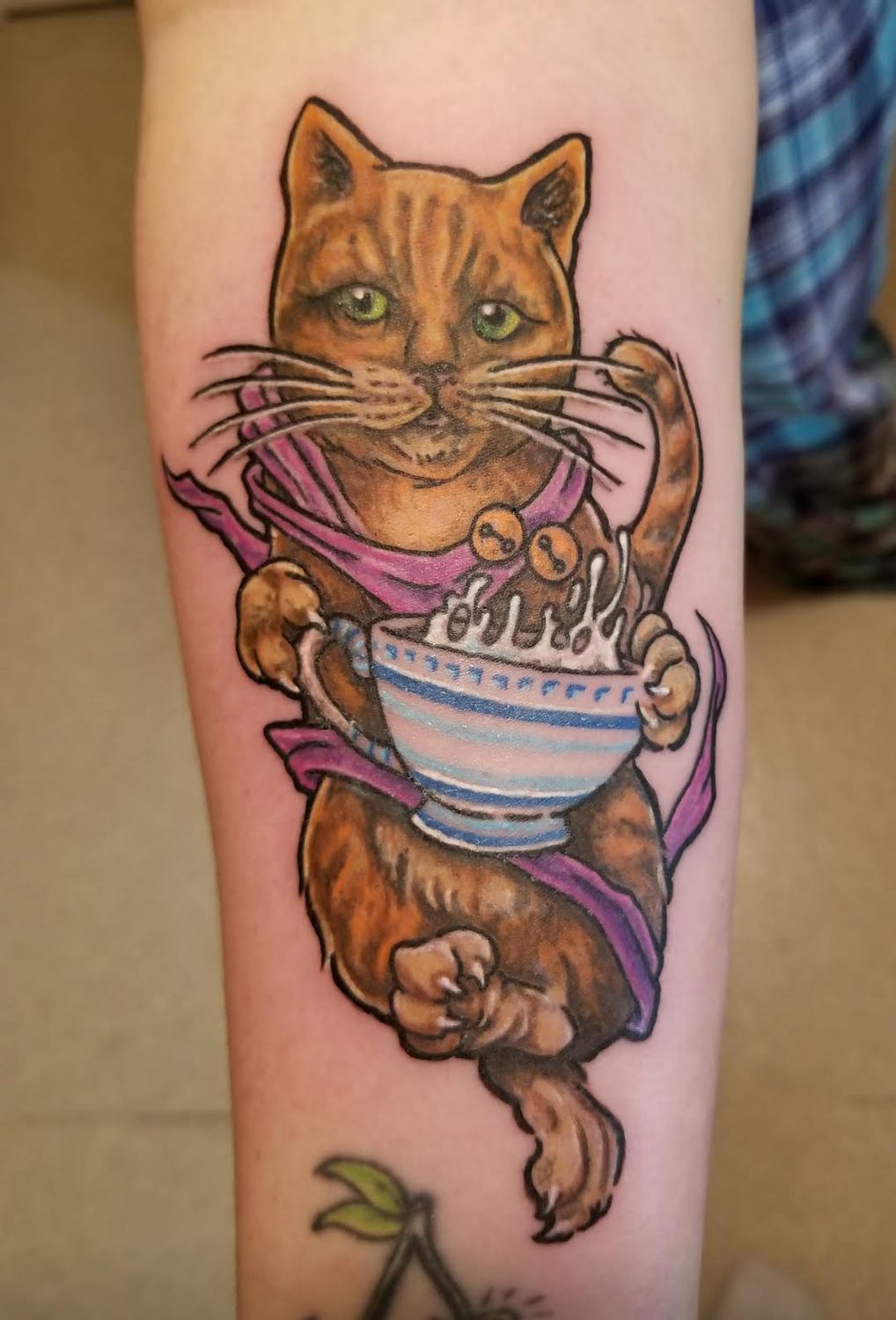 Colour orange tabby cat in a scarf cradling a steaming cup, forearm tattoo, Parksville BC