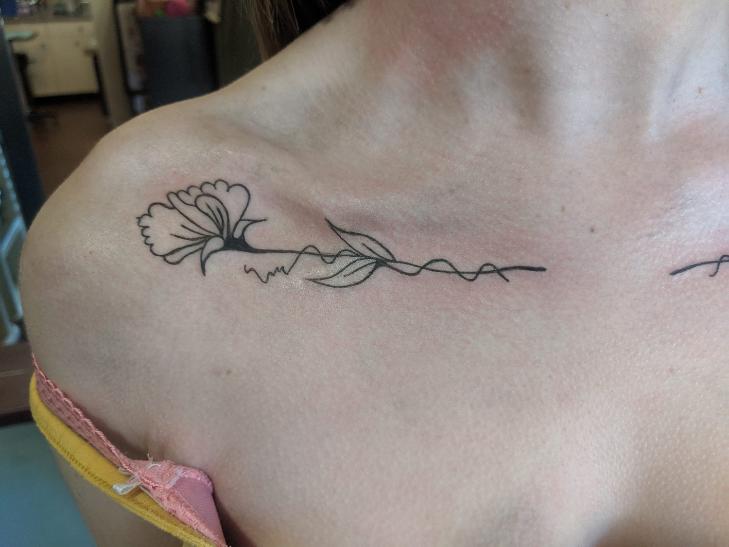 Fine line flower and trailing stem tattooed along the collarbone, Parksville BC