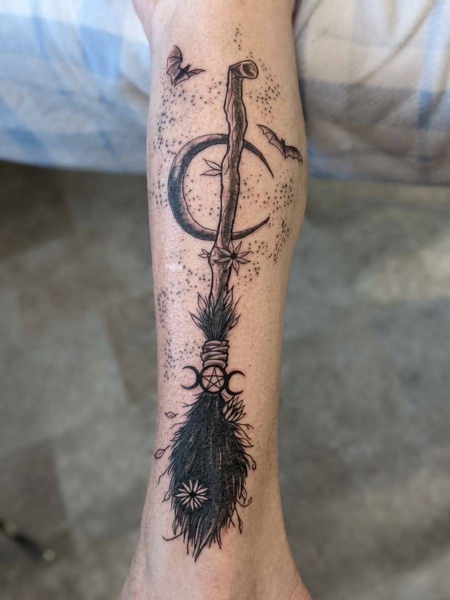 Black and grey witch's broom with a crescent moon and bats, forearm tattoo, Parksville BC